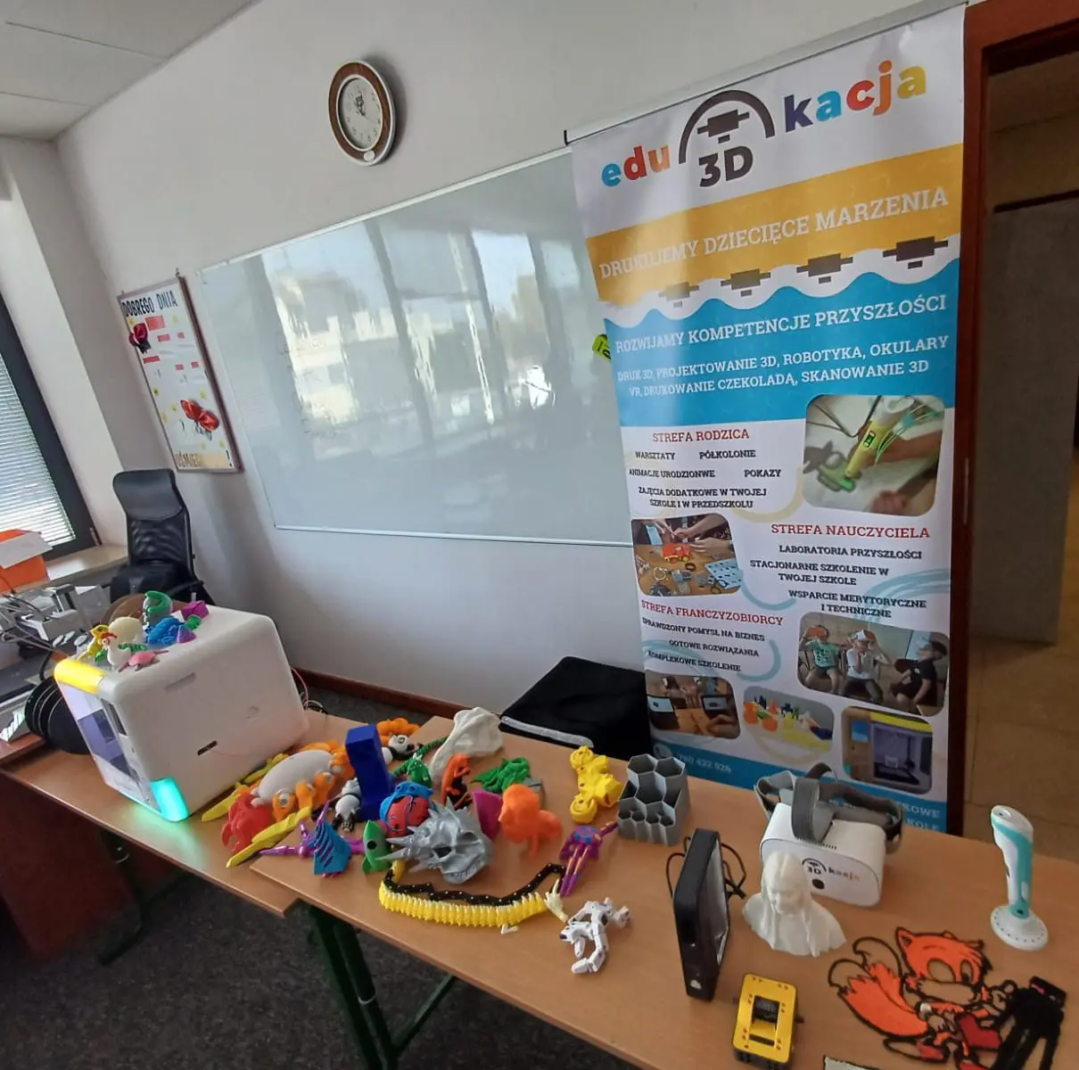 Stoisko Edu3Dkacja z wydrukami 3D, drukarką i długopisami 3D na stole