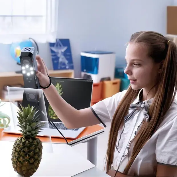 Uczennica skanuje ananasa ręcznym skanerem 3D, model widać na ekranie laptopa